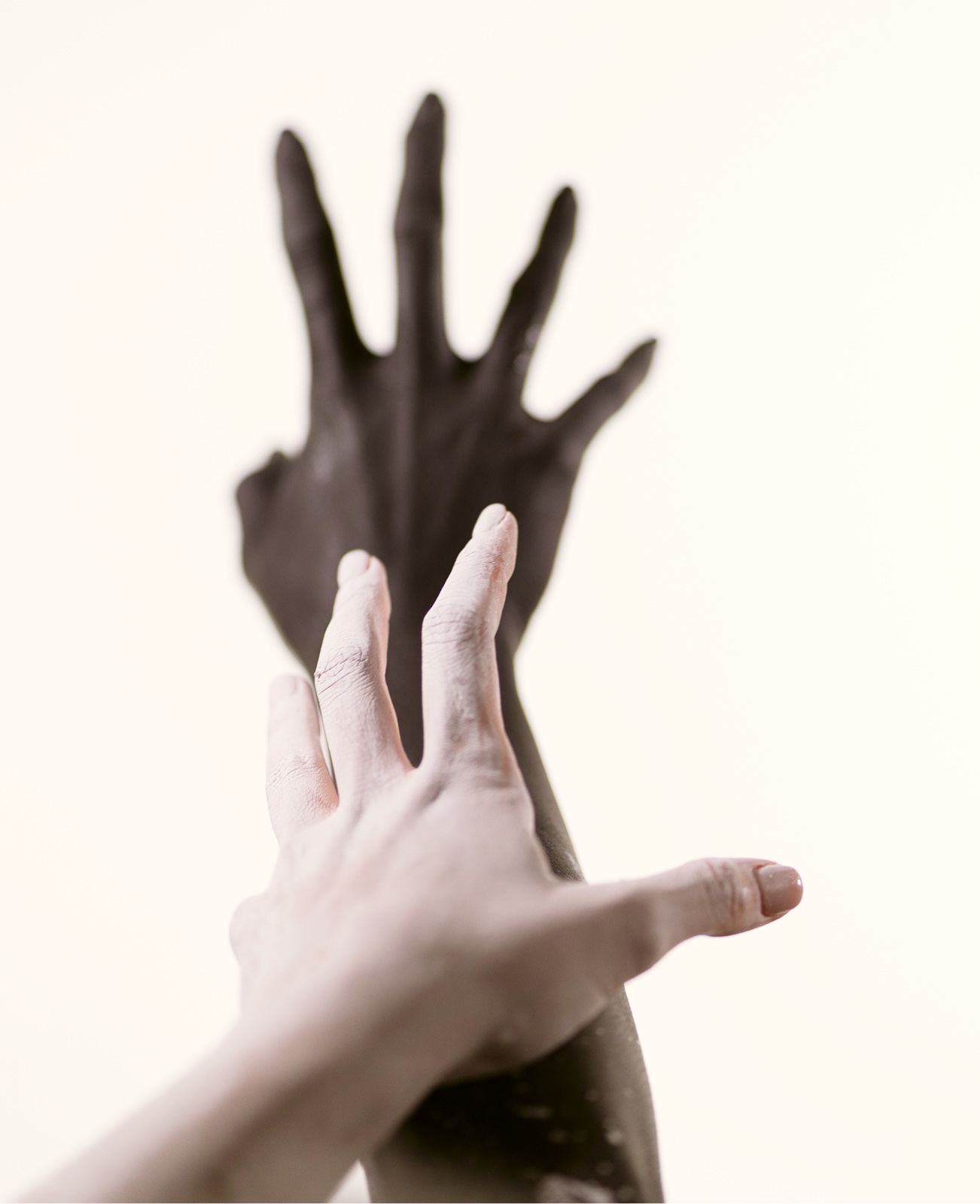Two painted hands reaching upward — one black, one white — embodying the album's duality
