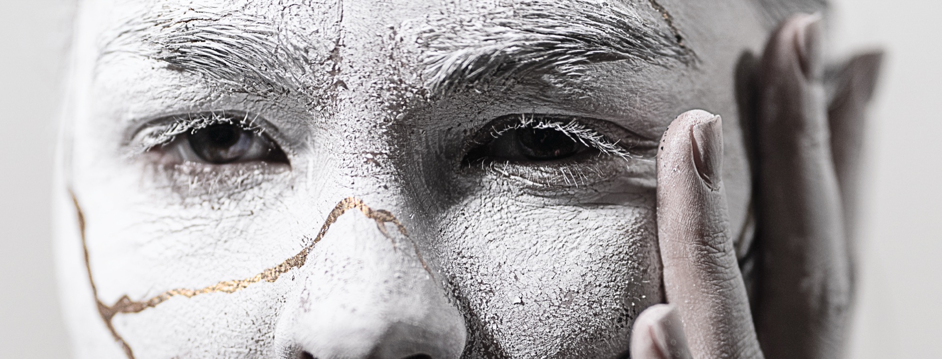 Close-up of the sculptural face — white concrete texture with gold kintsugi cracks running across the cheek and brow