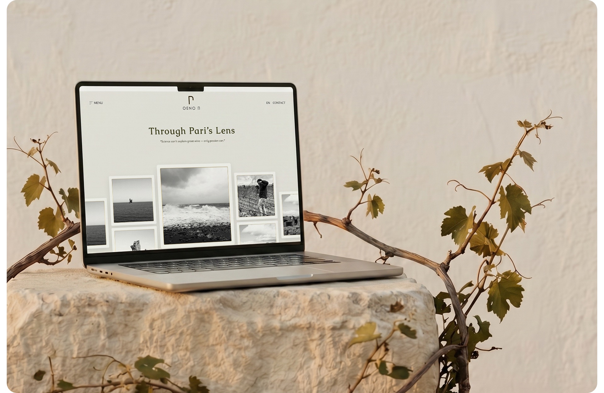 MacBook on a stone pedestal showing the OENO P 'Through Pari's Lens' gallery — black-and-white photographs of the island, vineyard and team