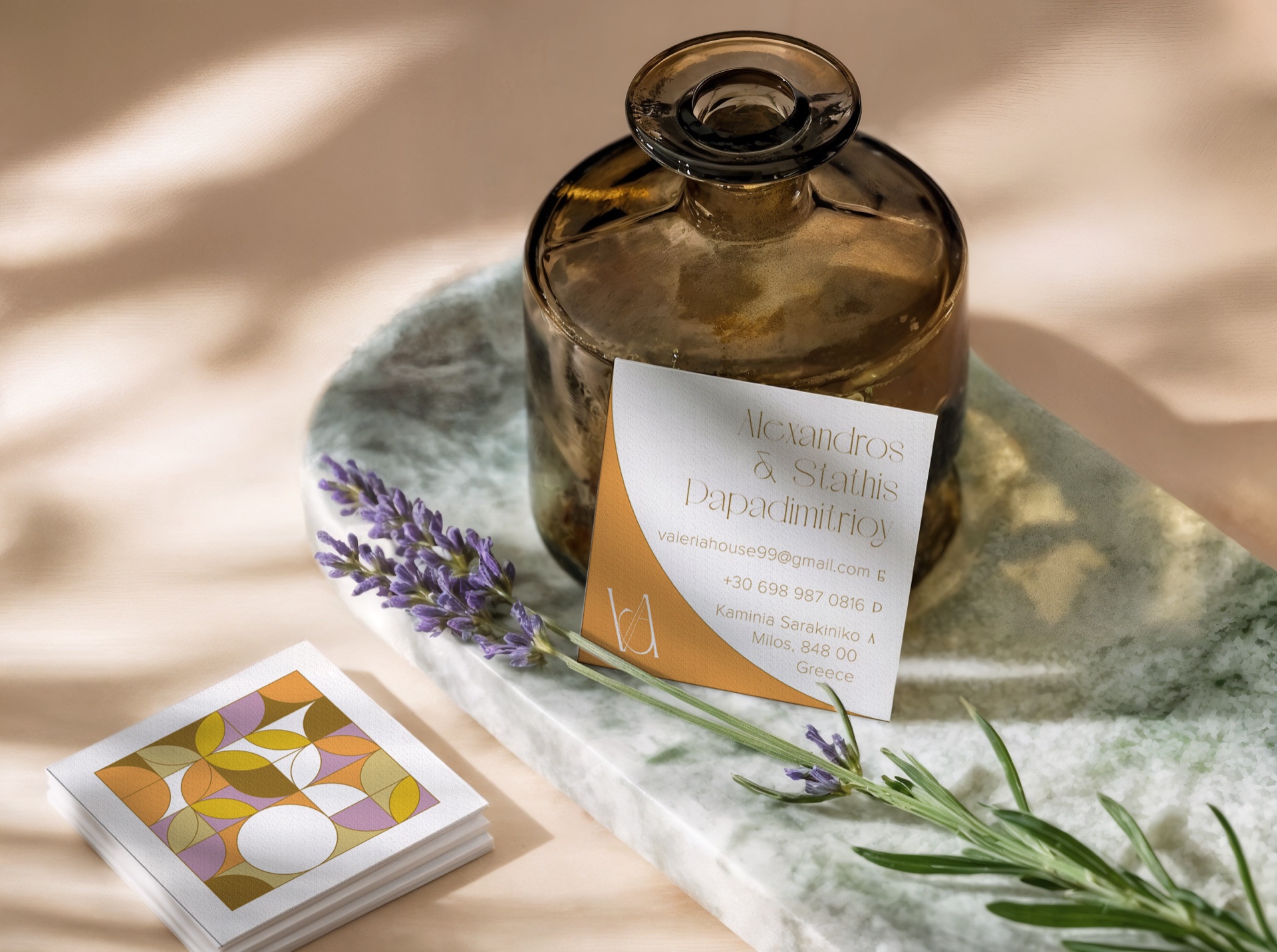 Stack of mosaic-printed Valeria's House business cards beside an amber bud vase, lavender sprigs and a personalised contact card on a marble tray