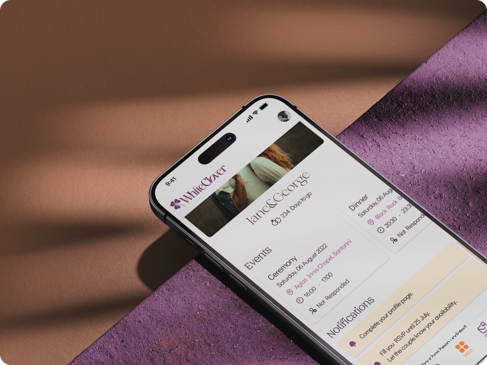 iPhone tilted between terracotta and purple shadows, showing the WhiteClover invitation screen for a couple's wedding