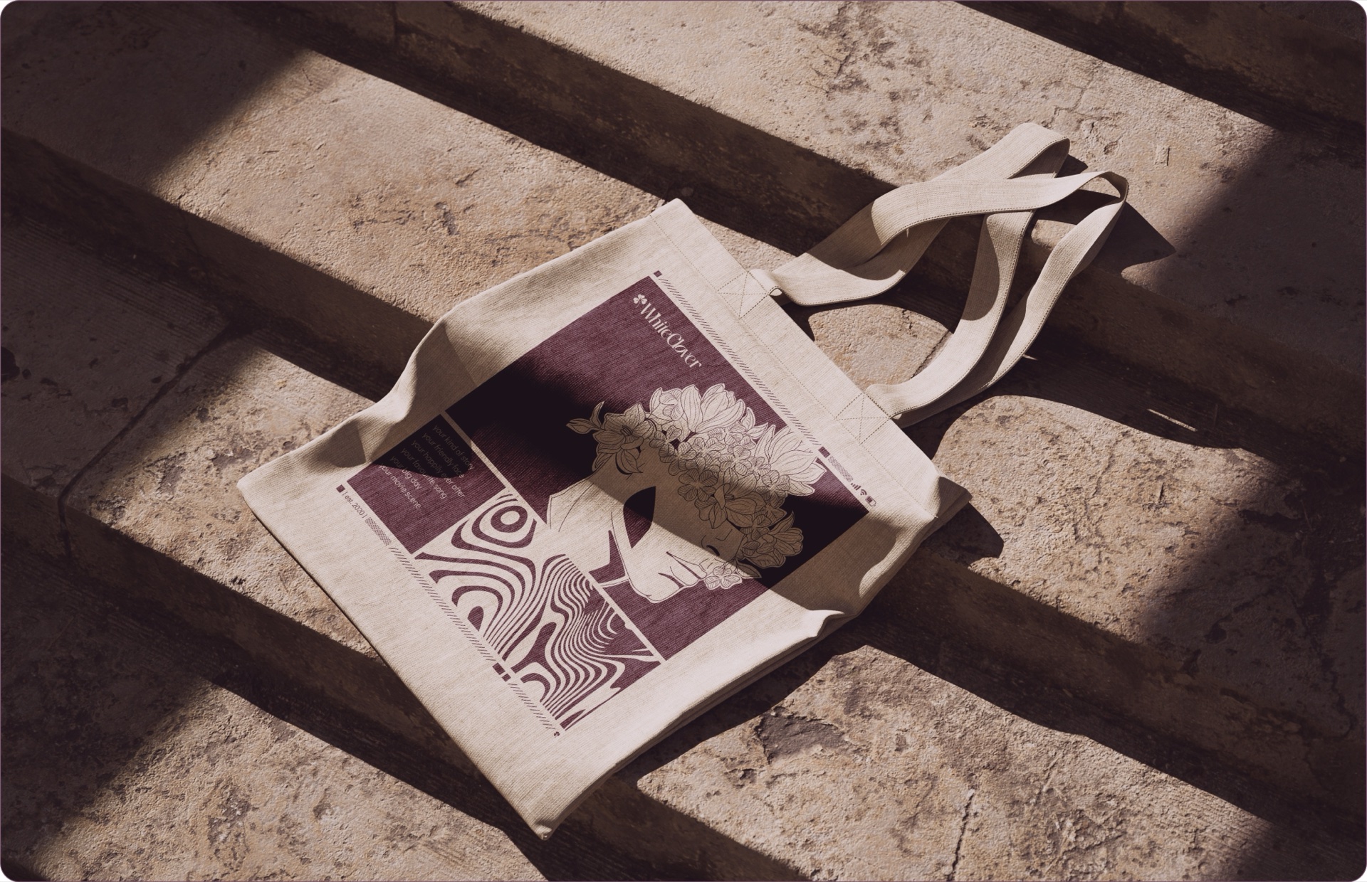 WhiteClover branded tote bag held over a wildflower meadow, showing the clover crest in detail